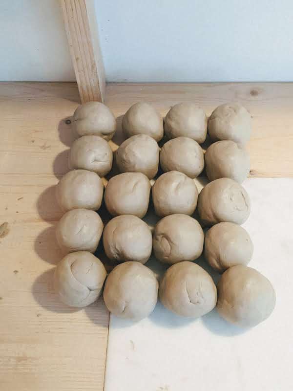 Balles de terre (grès blanc lisse) alignées et pétrie, prêtes à être tournées par l'artiste céramiste Pauline Krähenbühl